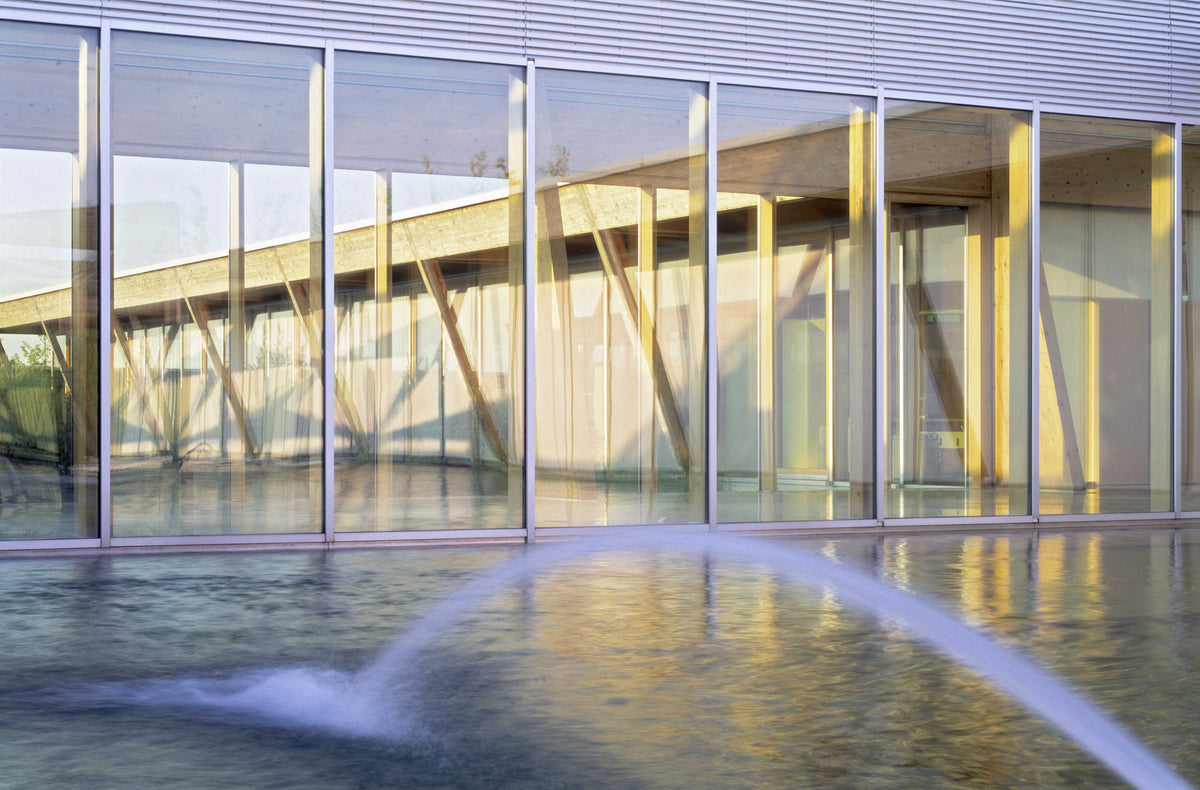 Modern glass building with wooden beams reflected in water.