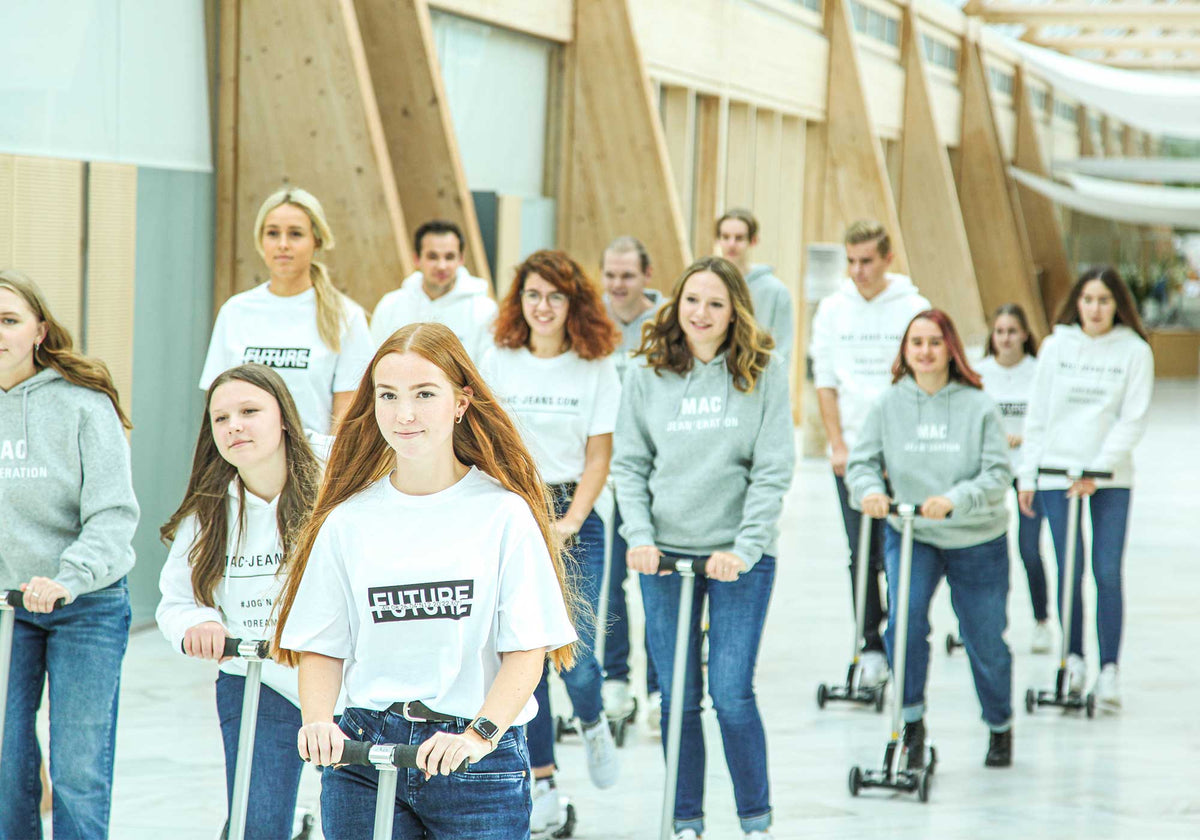 Young MAC employees riding scooters through the company atrium.