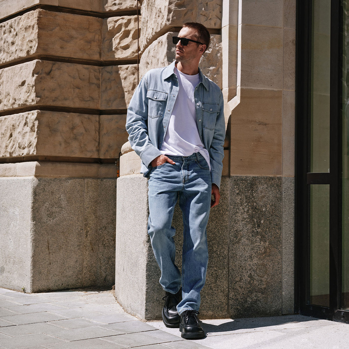 Man wearing light blue Rick jeans styled casually with a white T-shirt and denim jacket in an urban setting.