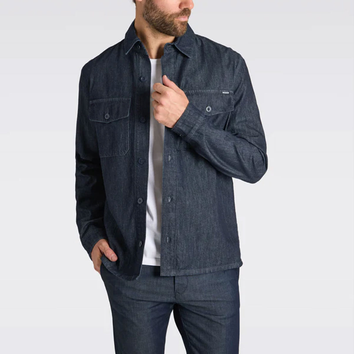 Man wearing a dark denim overshirt styled with matching jeans and a white T-shirt in a studio setting.