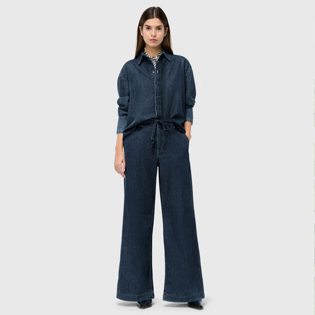 Woman wearing the Wendy denim jumpsuit with wide legs, styled cleanly against a neutral studio background.