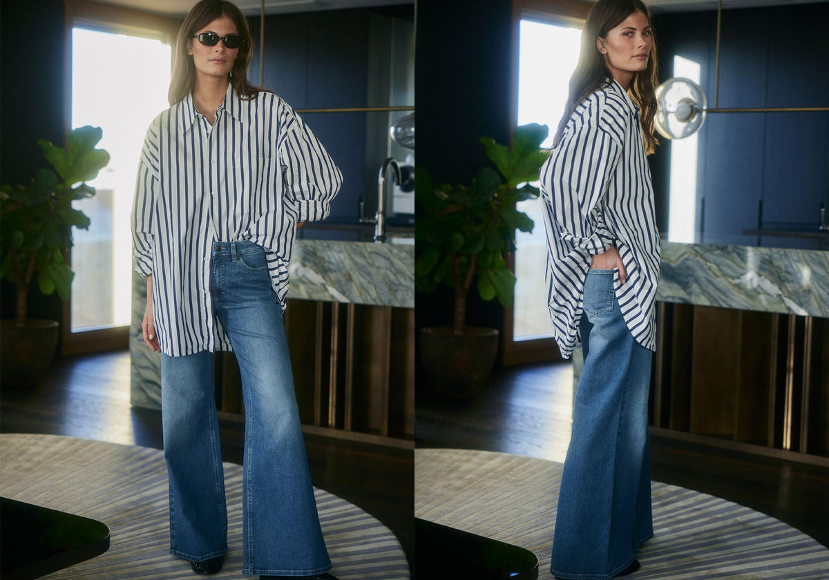 A woman in a striped oversized shirt and wide-leg blue jeans poses in a modern interior with natural light.