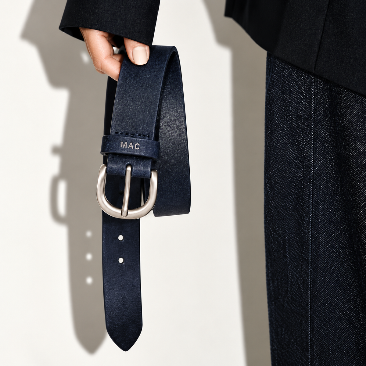 Woman holding a navy blue MAC leather belt with a silver buckle.