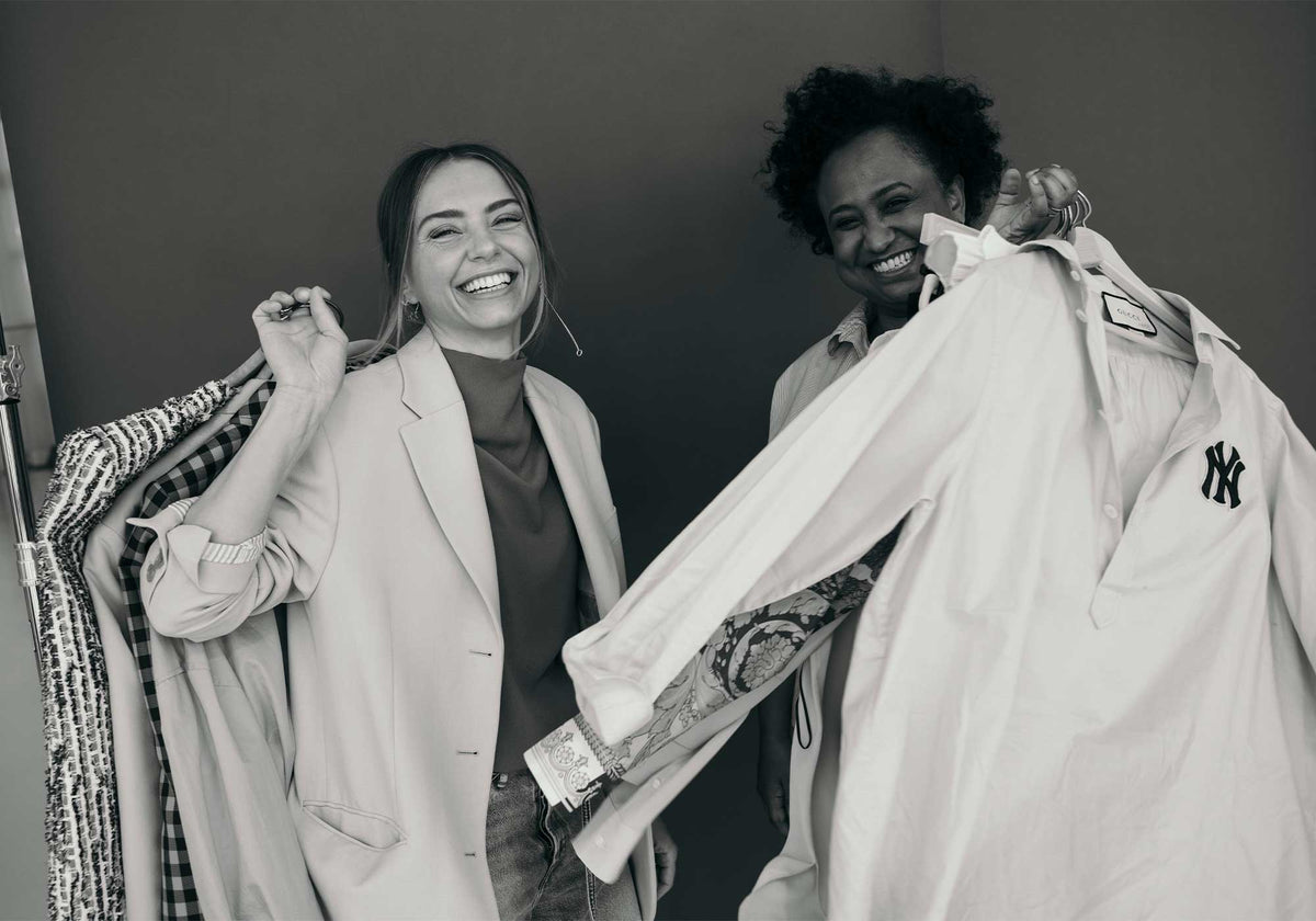 Two MAC designers smiling while presenting garments during a design fitting.