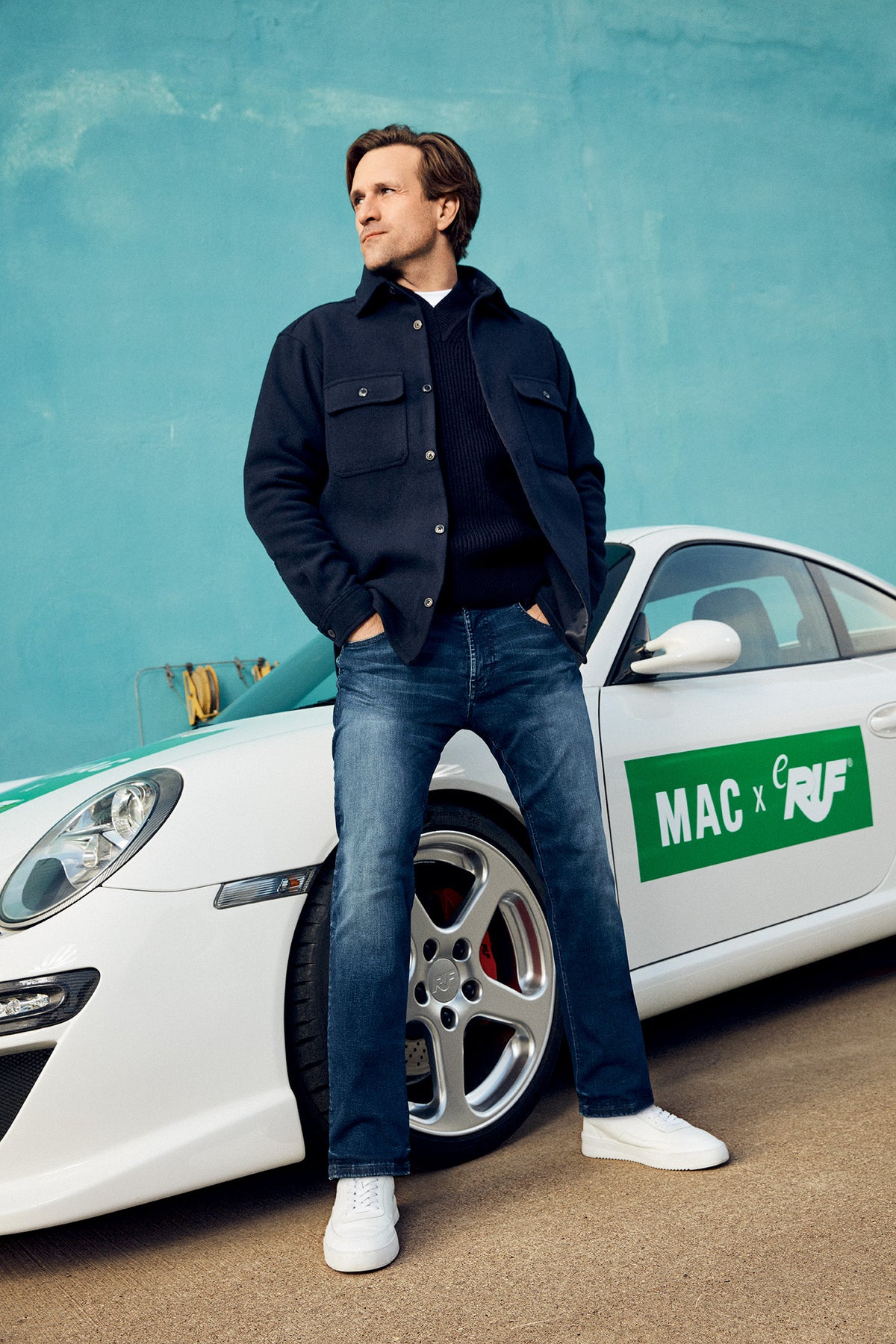 Men’s outfit featuring a dark jacket and MAC jeans in front of a sports car.