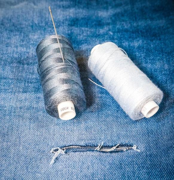 Close-up of sewing threads and needle placed on denim fabric, symbolizing professional jeans repair.